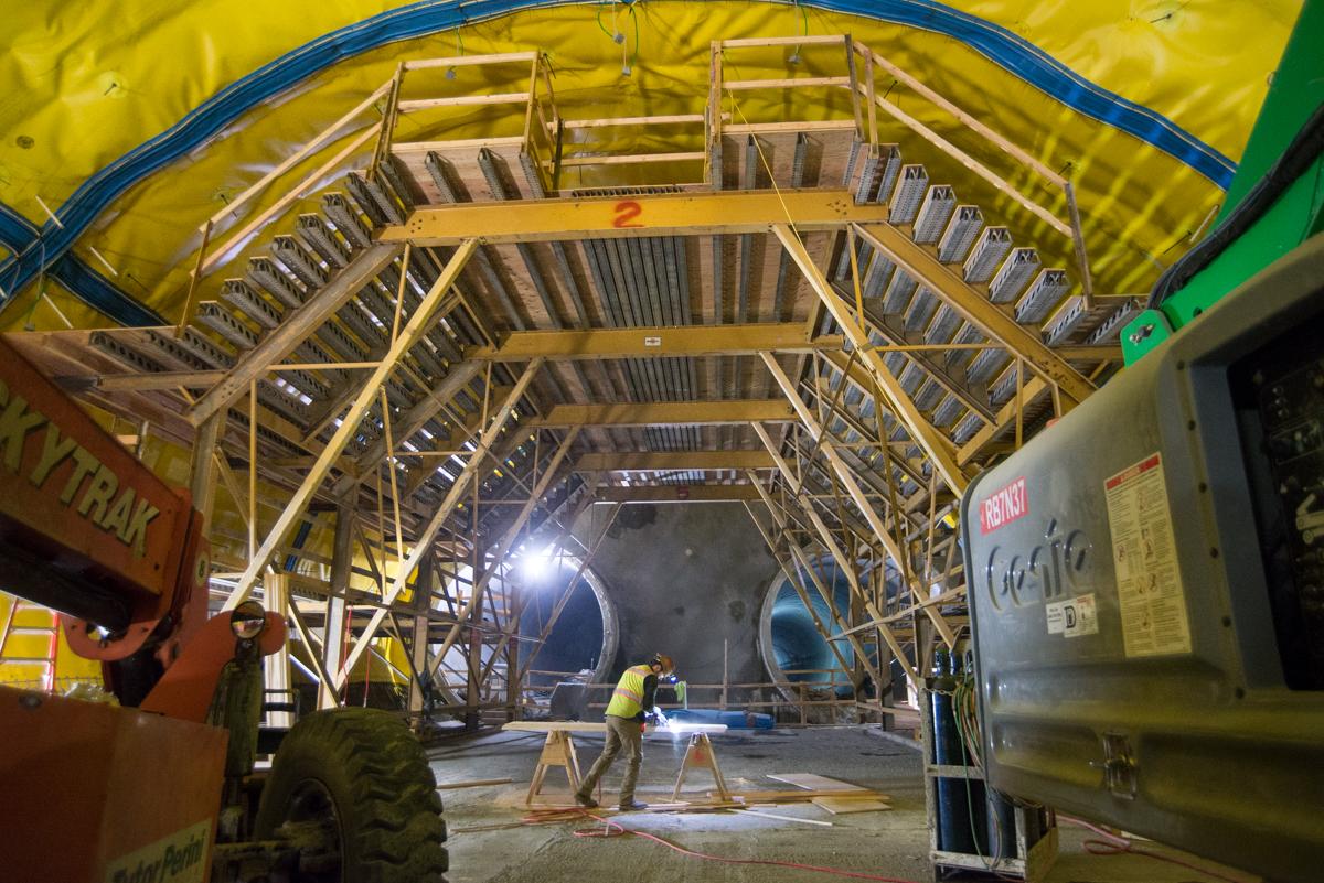 Interior view of underground transit tunnel with wooden scaffolding structure and construction equipment during night work.
