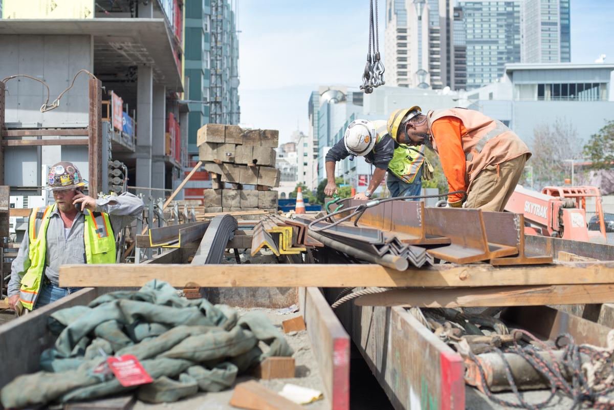 Construction workers prepare reinforcing steel for crane lifting at a downtown staging area.