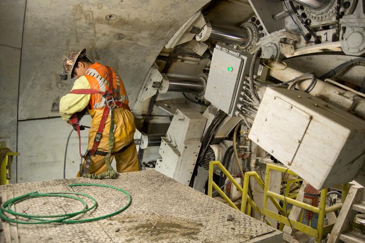 Worker in safety gear operating equipment inside subway tunnel under construction.