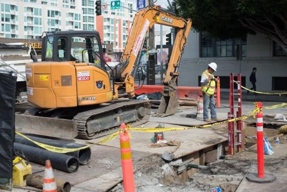 Construction excavator operating at 4th Street and Brannan Street with safety barriers and workers present.
