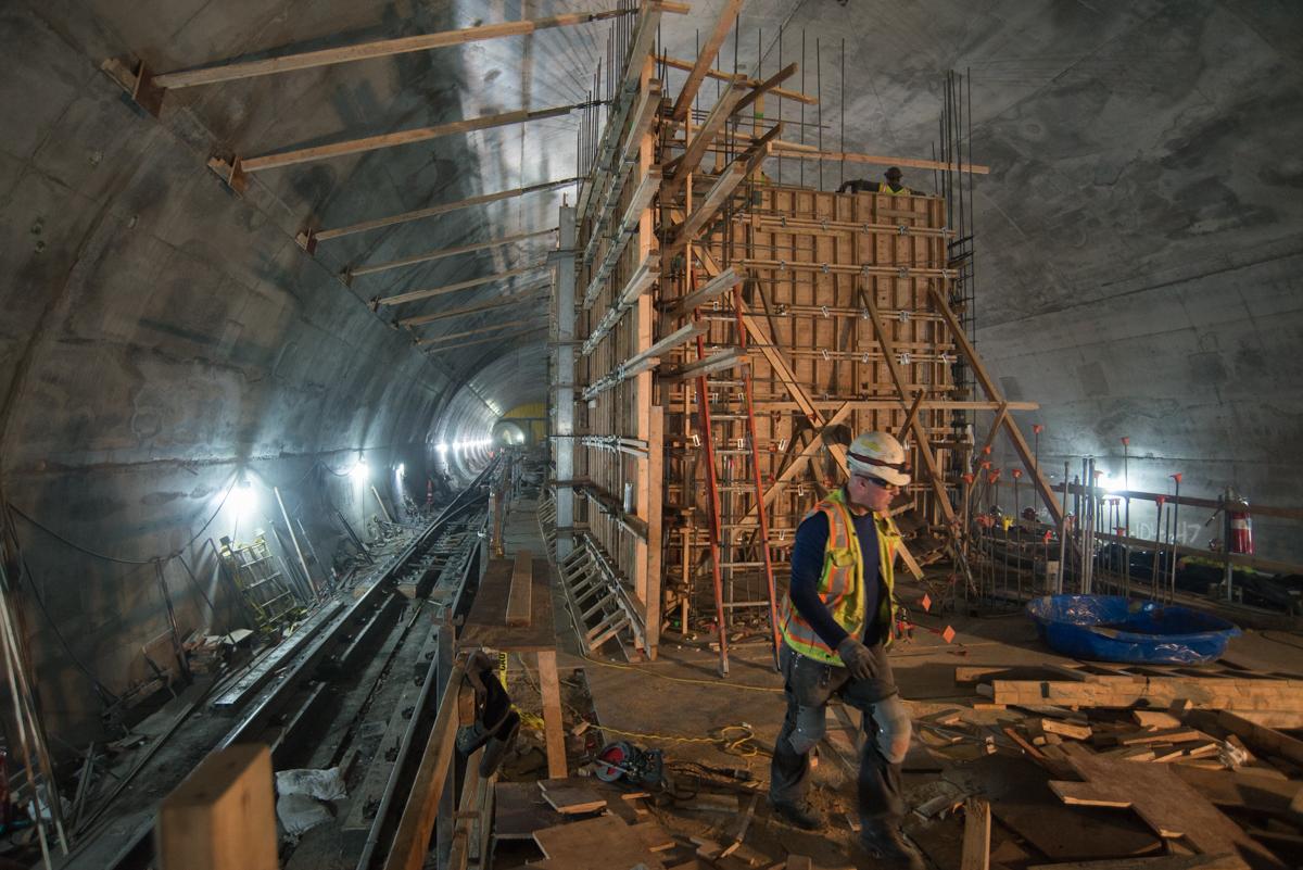 Workers in safety gear inside a subway tunnel under construction with wooden formwork and steel reinforcement visible.