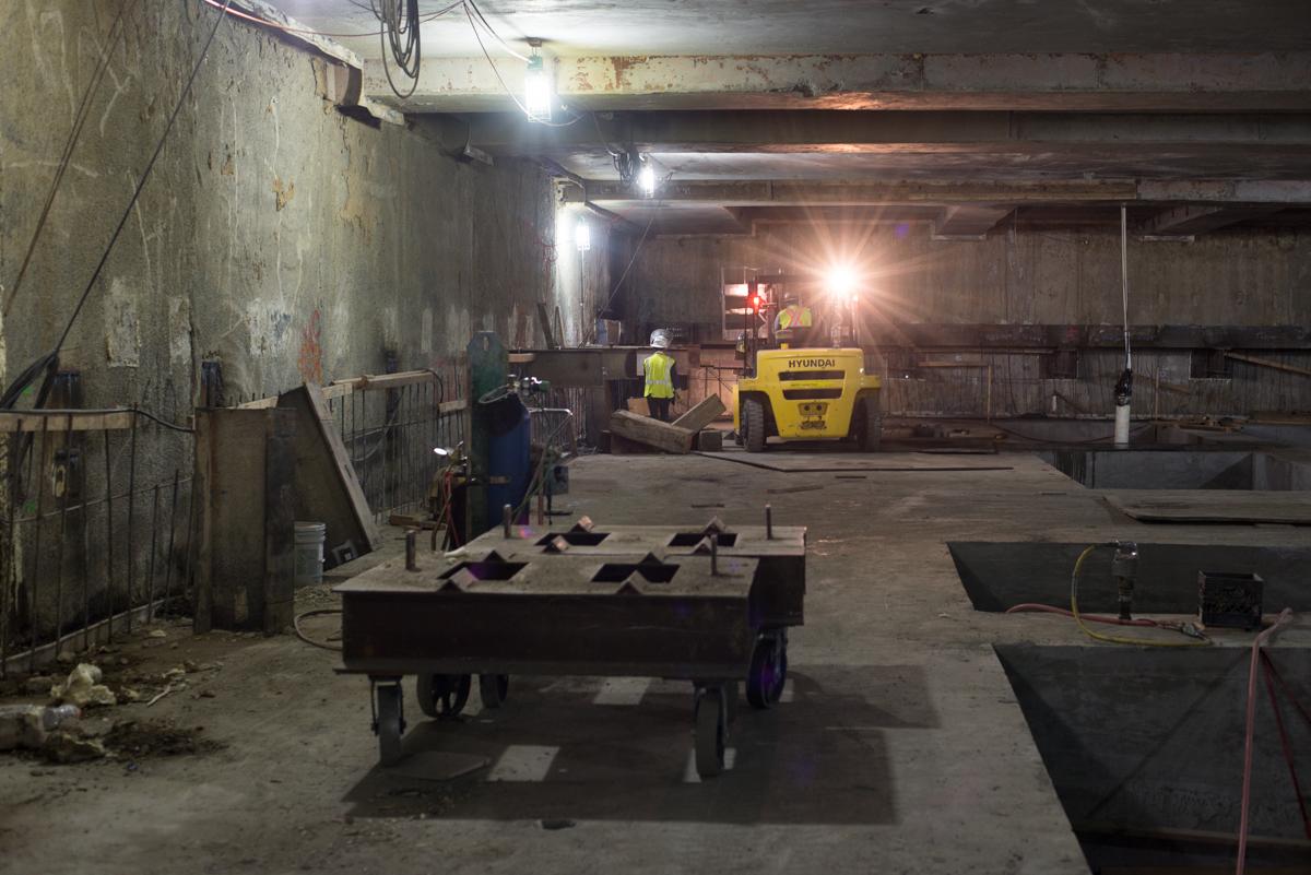 Industrial underground transit station under construction with yellow forklift and metal bracing equipment.