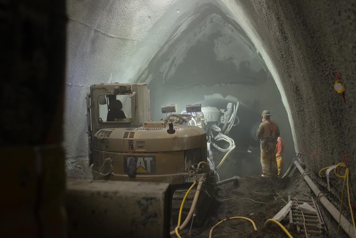 Workers in protective gear inspect shotcrete reinforcement in an underground transit tunnel during construction.