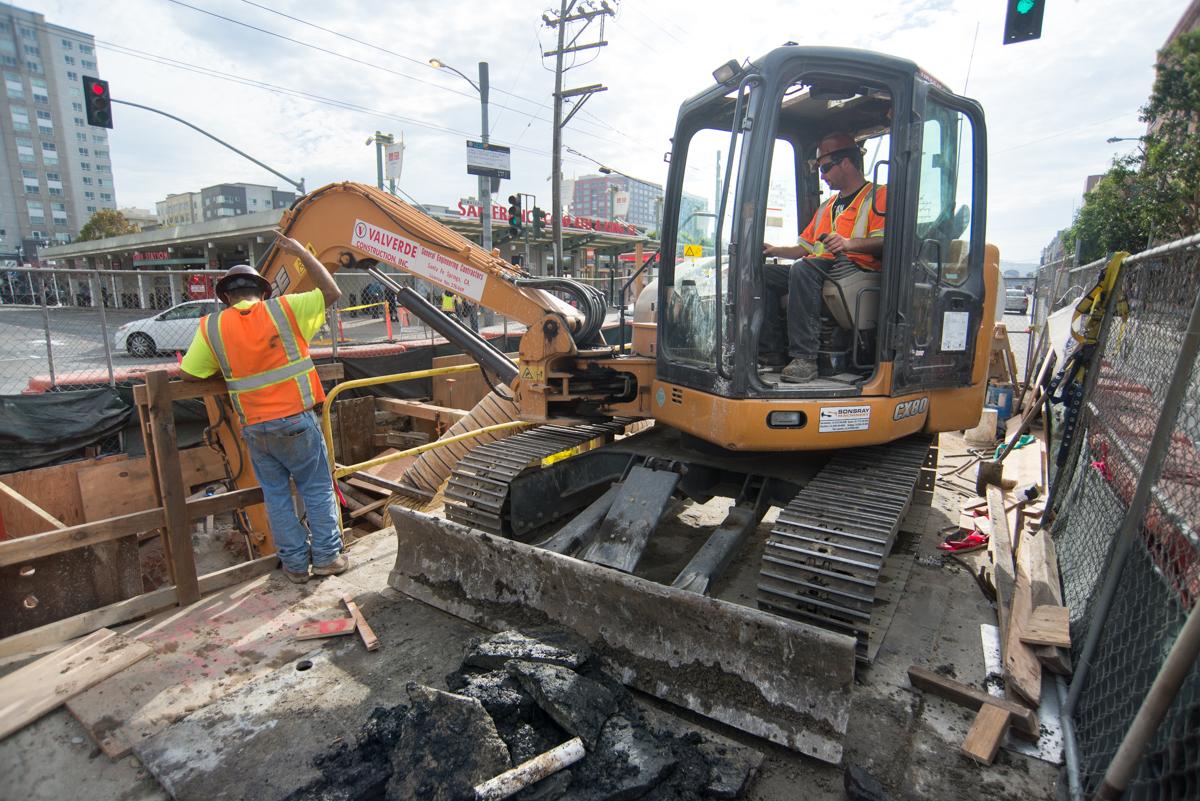 Construction worker operating excavator at 4th and Townsend manhole structure site for Central Subway project.