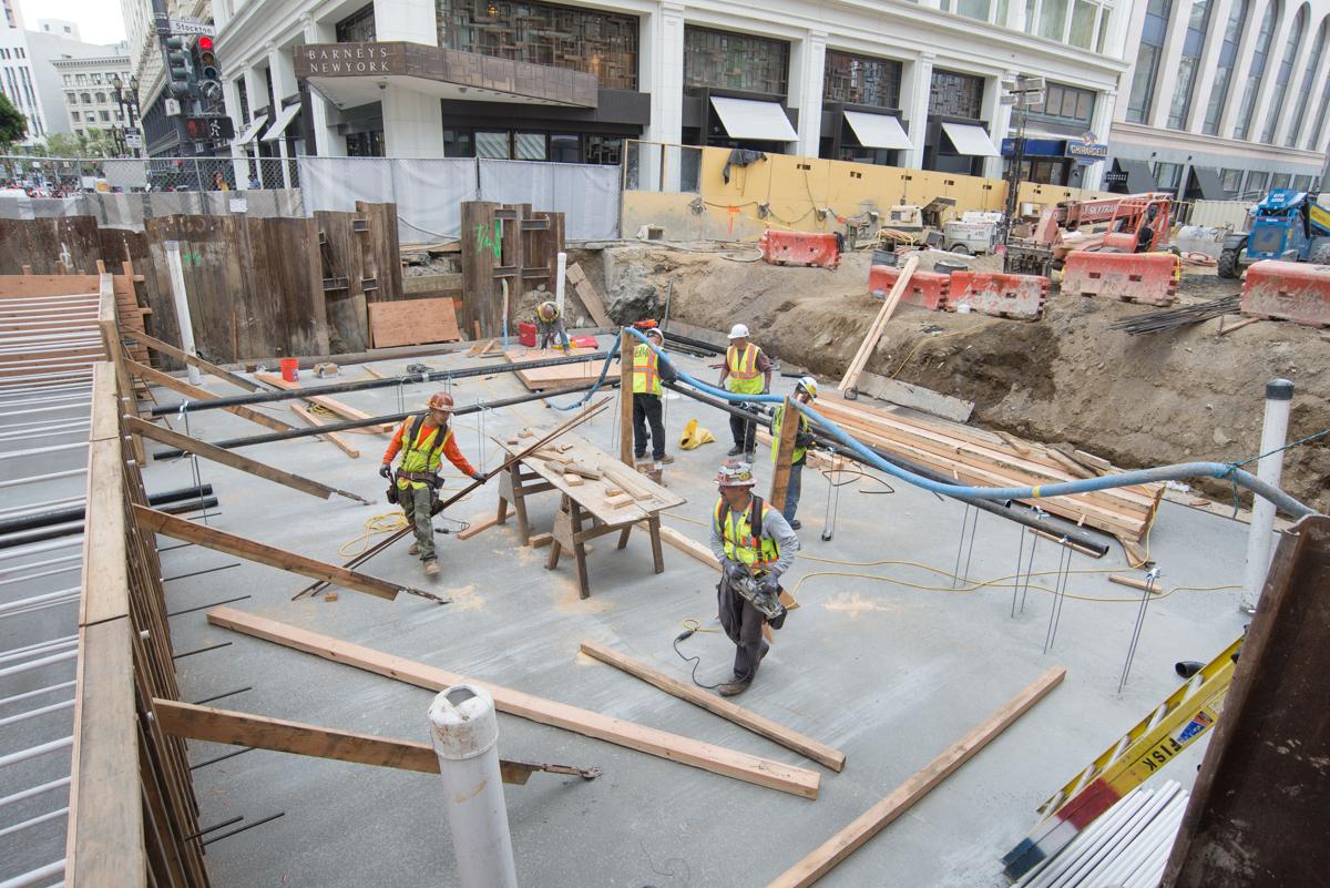 Construction workers in safety vests work on concrete foundation at O'Farrell and Stockton intersection.