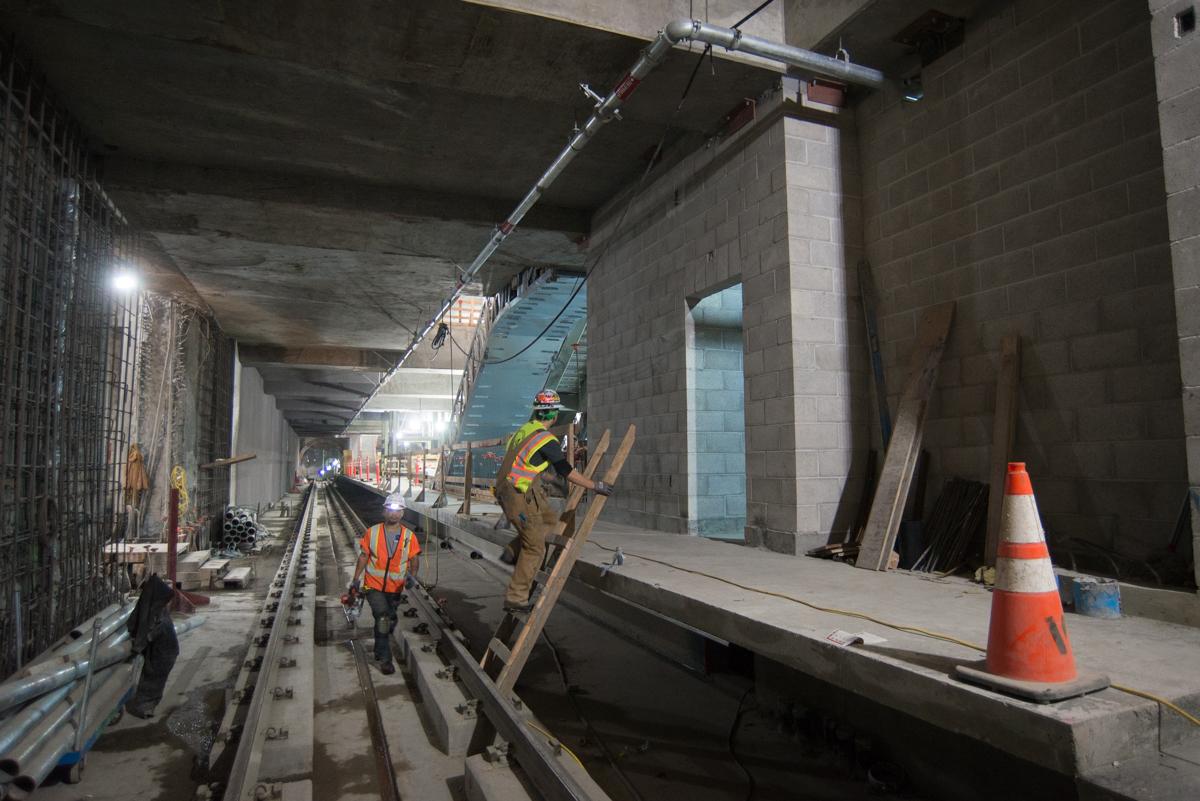 Construction workers in safety gear work on interior walls and structural elements inside an underground transit station under development.