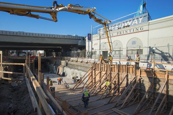 Construction crew pouring concrete walls for subway portal using pump truck at 4th Street station site.