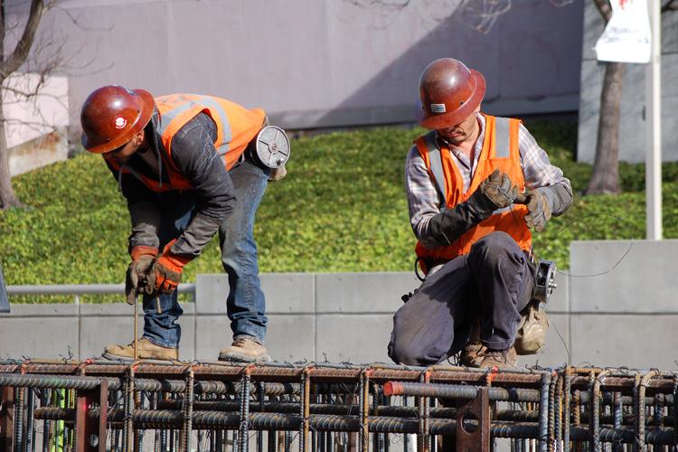 Two construction workers in hard hats and safety vests working with rebar reinforcement on 4th Street.