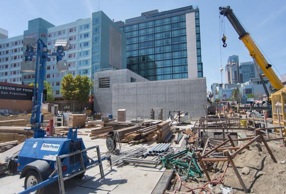Active construction site at Yerba Buena/Moscone Station with concrete headhouse structure, cranes, and equipment surrounded by urban buildings.
