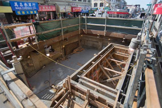 Construction pit showing completed north egress shaft for Chinatown Station with wooden framing and urban street visible above.