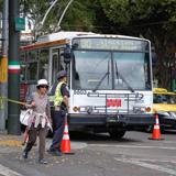 Bus stopped at intersection with pedestrians and traffic cones nearby during street construction.