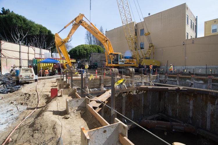 Construction site with yellow excavator, wooden shoring, and crane at tunnel boring machine retrieval shaft.