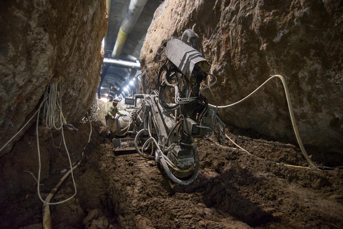 Excavator with shotcrete spraying equipment working in underground tunnel during utility upgrade construction.