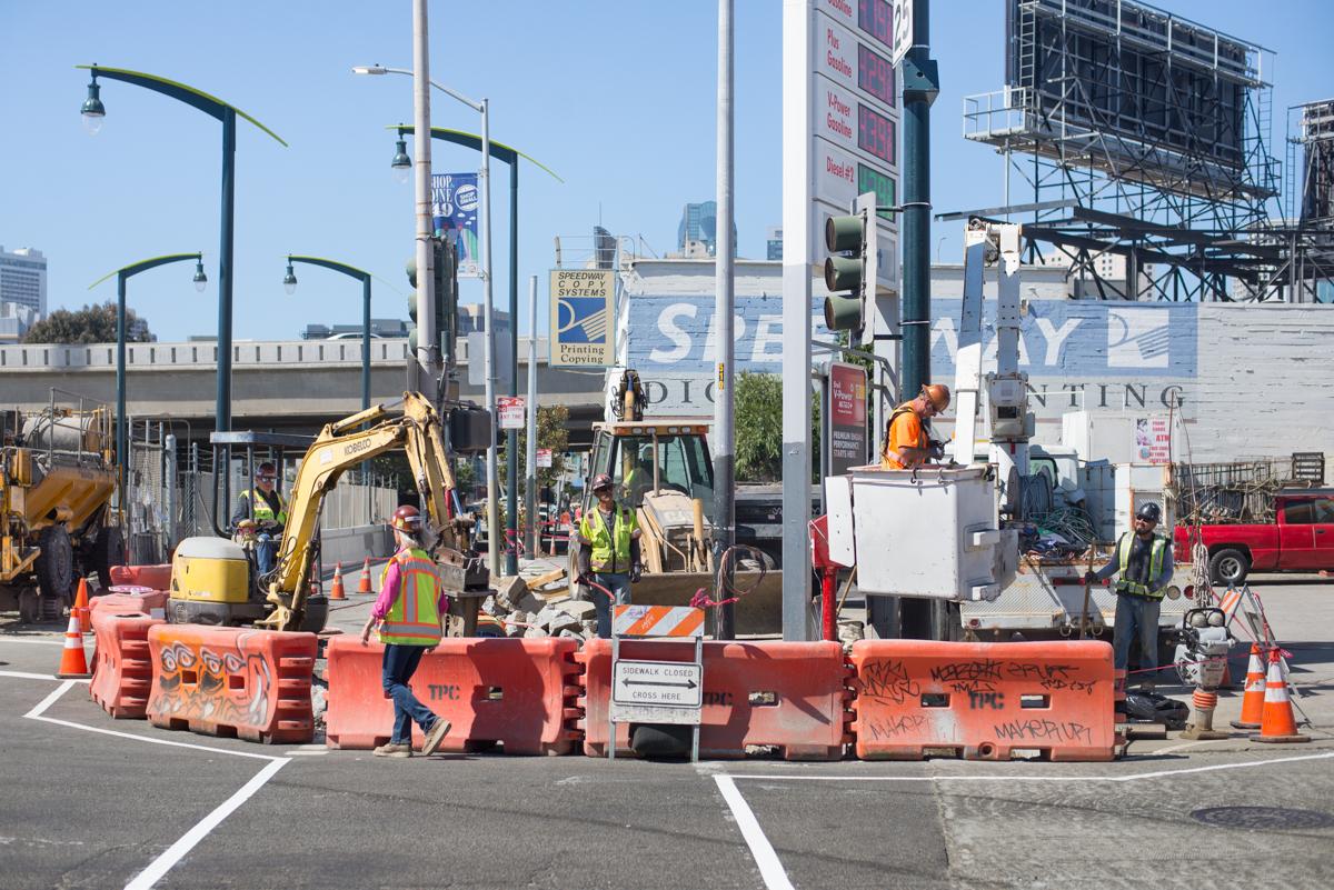 Construction work at 4th and Bryant with heavy equipment, barriers, and workers in safety gear.
