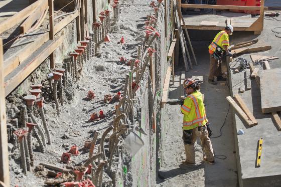 Construction workers in safety vests work on concrete wall formwork at Chinatown Station site.