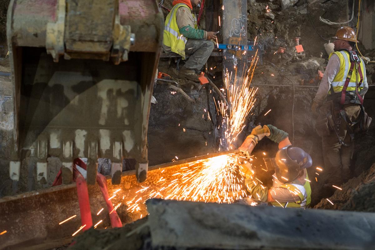 Workers use an angle grinder on steel beam during underground structural repairs on Stockton Street.