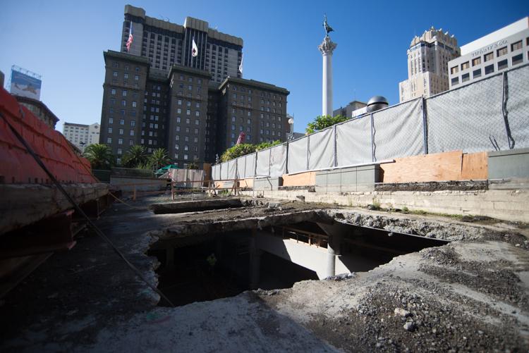 Construction site at Union Square with excavated holes in garage roof, protective fencing, and downtown buildings in background.