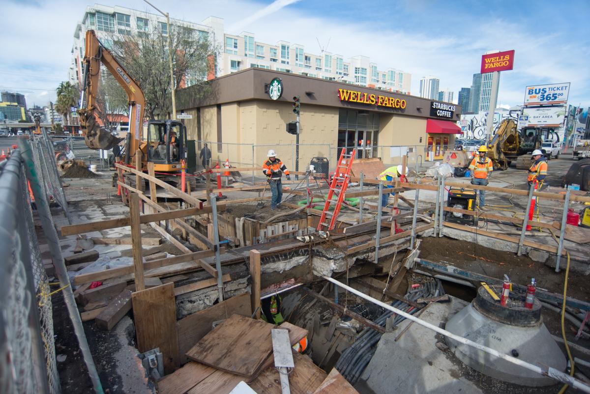 Construction crew performs utility work at 4th and Brannan intersection with excavation equipment and safety barriers.