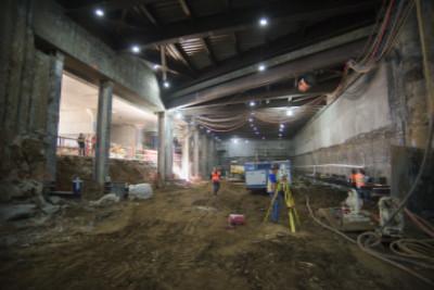 Underground construction site with workers, equipment, and exposed concrete walls under bright lighting.