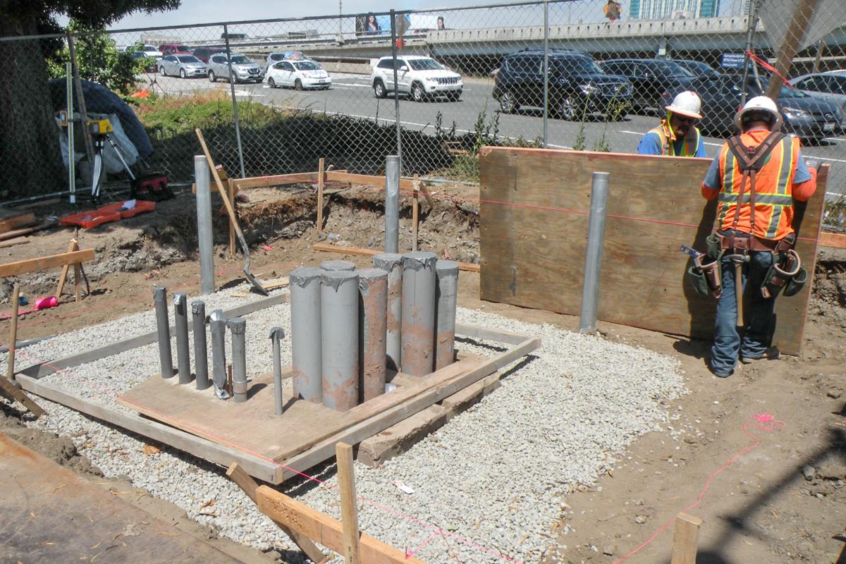 Construction workers in safety gear install concrete forms for a breaker panel foundation at a transit station work site.