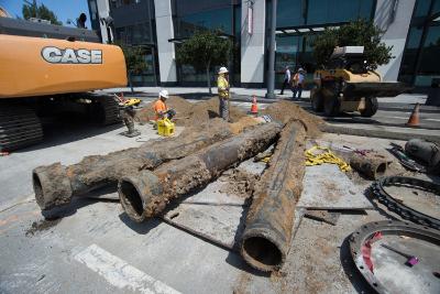 Old sewer pipes removed during utility work on 4th Street with construction equipment and crew visible.