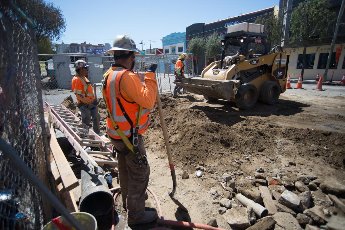 Construction workers perform sewer slip lining work on 4th Street, with heavy equipment and excavation visible.