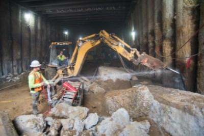Construction worker operating excavator to demolish concrete walls underground at transit station.