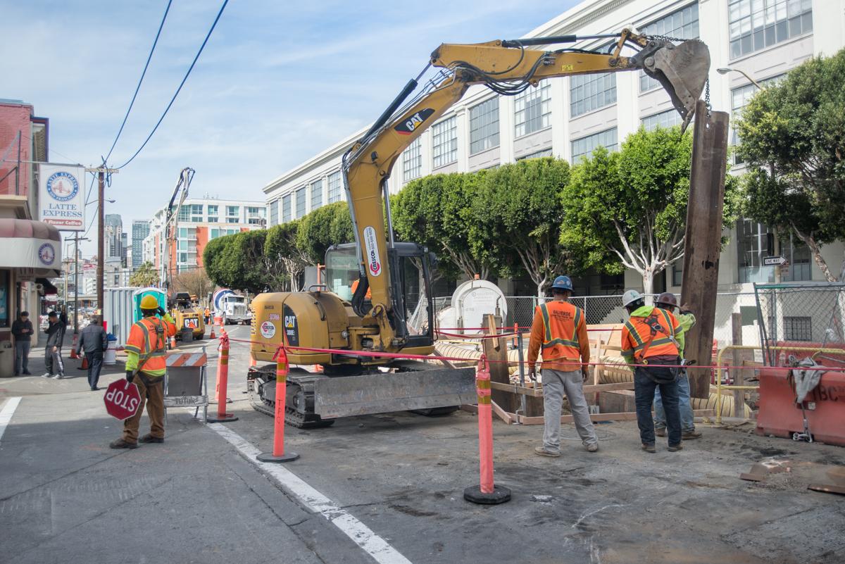 Construction crew operates excavator to install steel sheet piles at 4th and Bluxome Street.