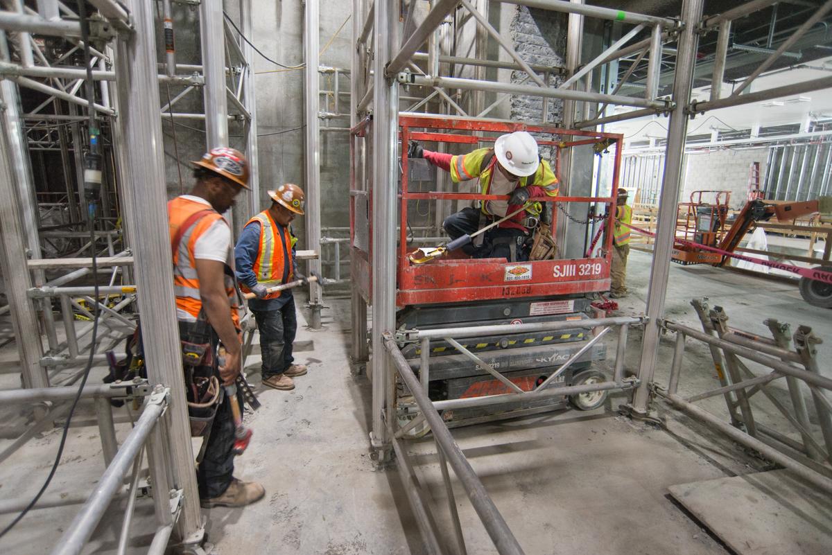 Construction workers remove scaffolding from transit station using scissor lift and hand tools.