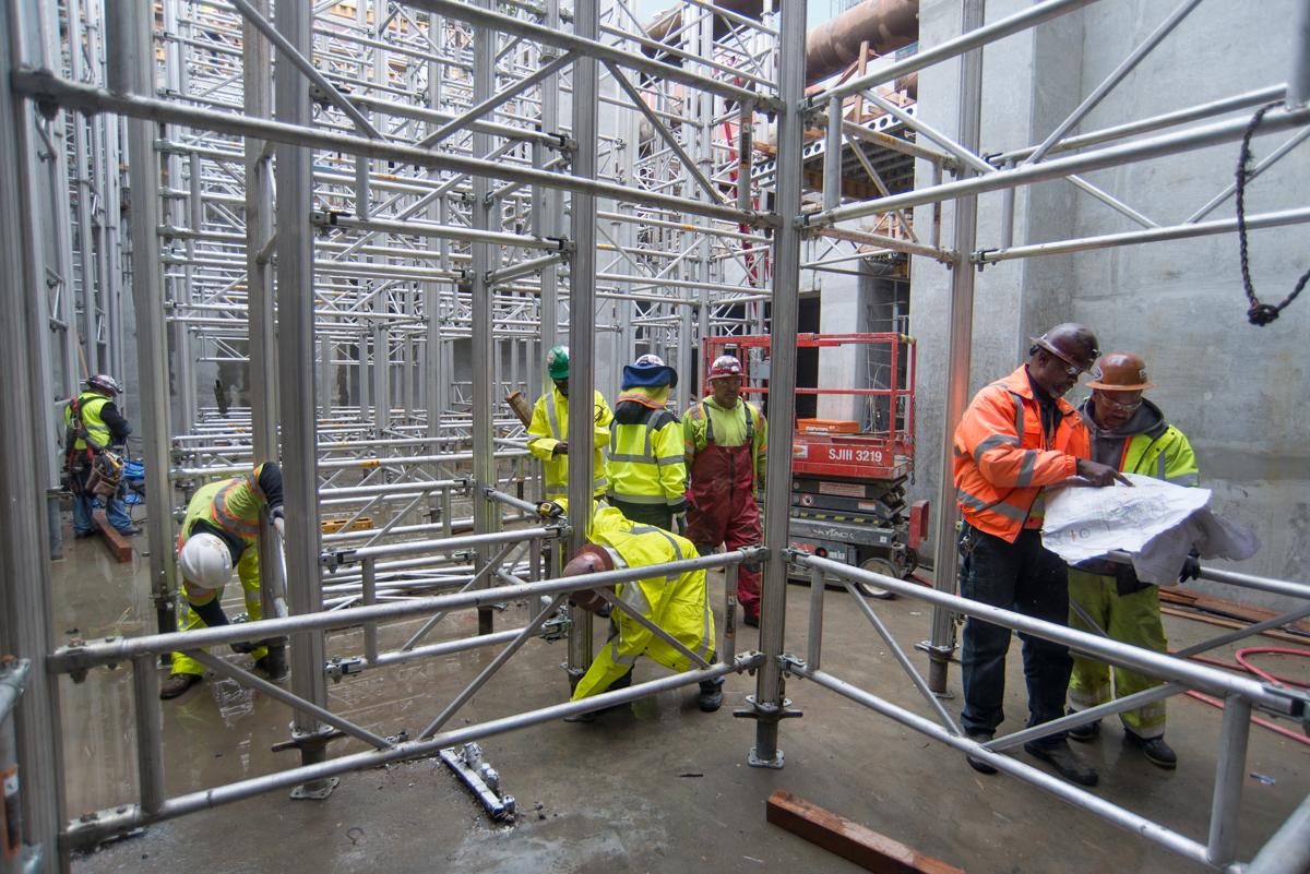 Construction workers in safety gear assembling metal scaffolding inside a concrete structure.