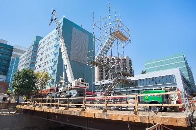 Construction site with scaffolding, excavation, and utility work near urban buildings and transit infrastructure.