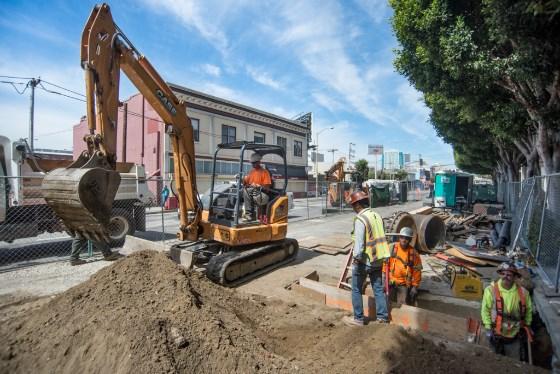 Construction crew operates excavator for Central Subway sewer line installation on 4th Street.