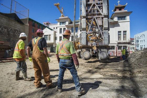 Construction workers in safety gear observe drilling equipment at the future Chinatown Station site on Stockton Street.