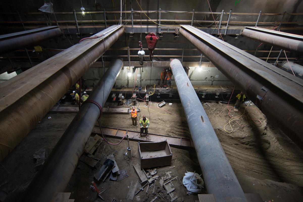 Workers in safety gear install structural steel bracing inside a deep underground station excavation at Union Square.