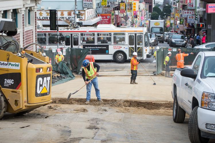 Construction workers and equipment on Washington Street at Stockton, with transit bus and city street in background.