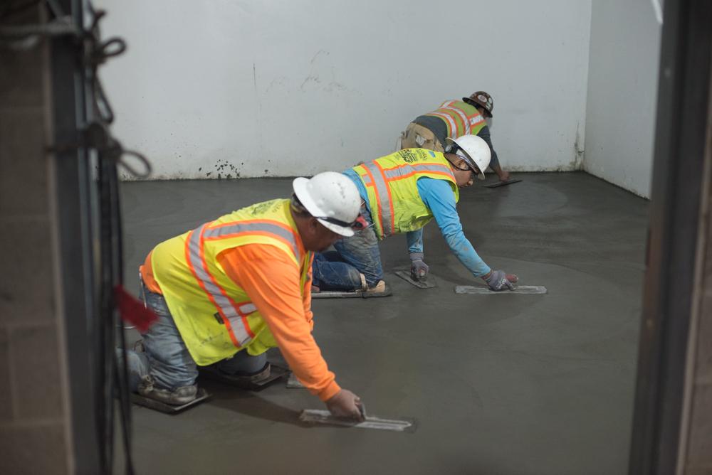 Construction workers smooth concrete floor slab inside transit station headhouse