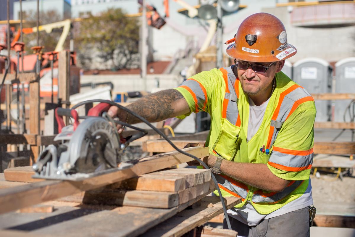 Construction worker using circular saw on wooden beam at transit station work site.