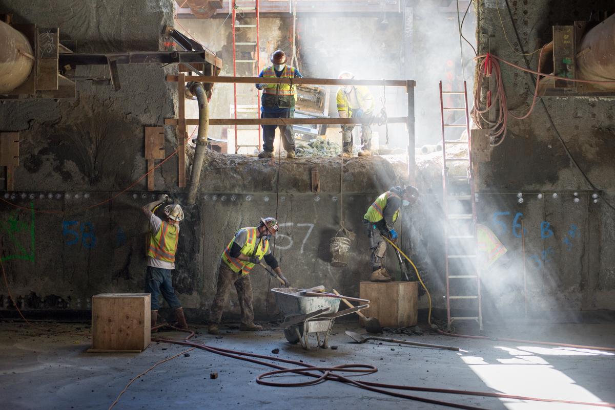 Workers in safety vests use high-pressure water jets during underground station construction excavation.