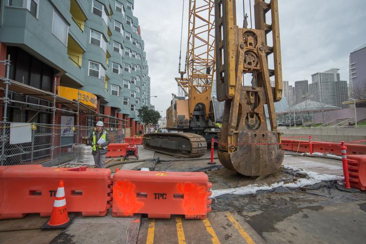 Construction site on 4th Street with clamshell excavator, red barriers, and nearby apartment building