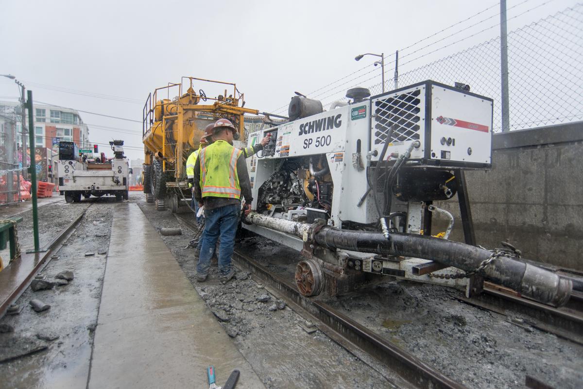 Construction workers maintain a concrete pump truck during heavy rain at a tunnel portal work site.