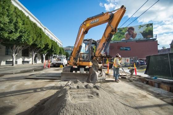 CASE excavator operating on urban street during Central Subway construction work, with workers and equipment visible.
