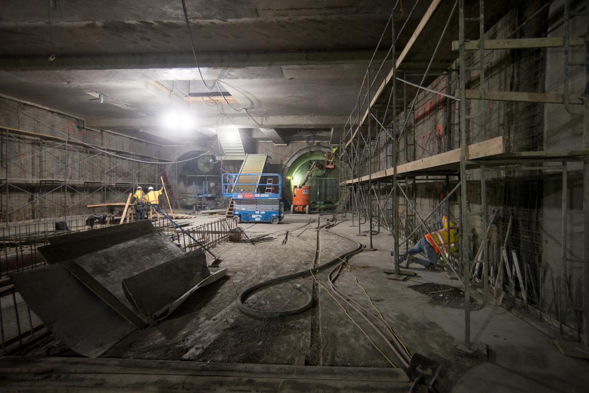 Construction workers install rebar and steel mesh inside an underground transit station platform using scaffolding and equipment.