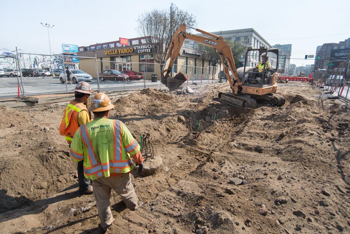 Construction workers and excavator uncovering foundation piles at 4th and Brannan station platform work site.