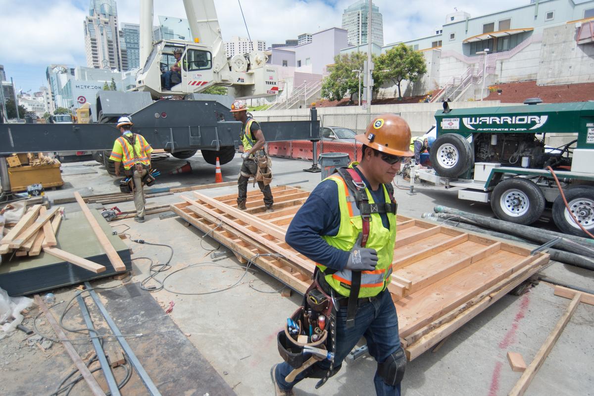 Construction workers assemble wooden forms for concrete beam work at 4th Street transit site.