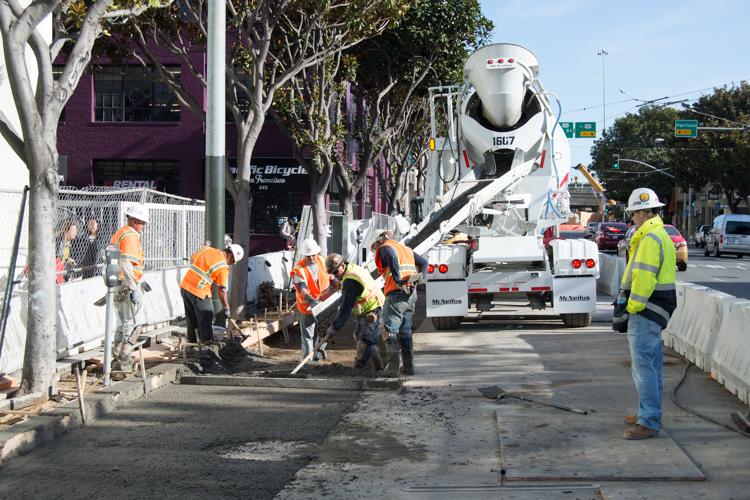 Construction crew pours concrete on 4th Street while cement truck stands by and workers direct traffic.