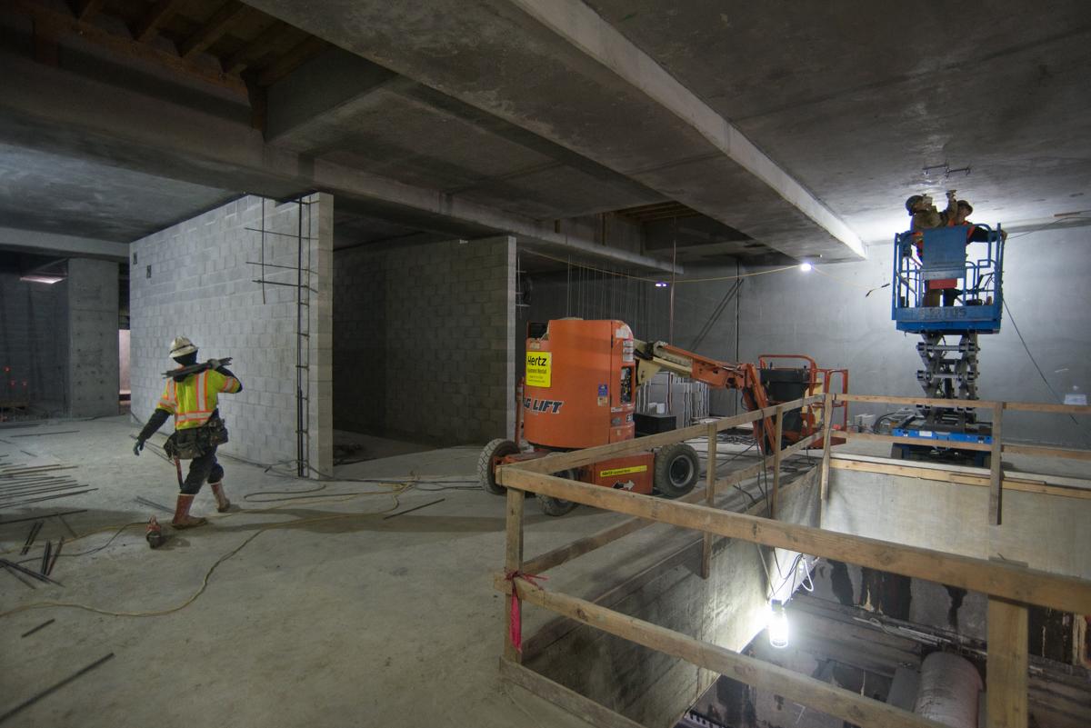 Construction workers on elevated lift and ground level inside underground transit station box with concrete walls and ceiling beams.