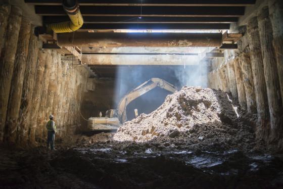 Light streams through tunnel opening as excavator works on Union Square station construction.