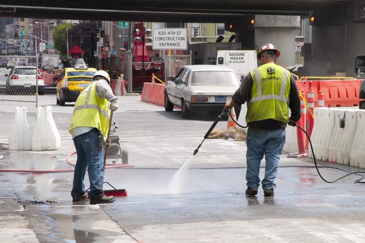 Workers in safety vests pressure wash a street section on 4th Street during roadway restoration work.