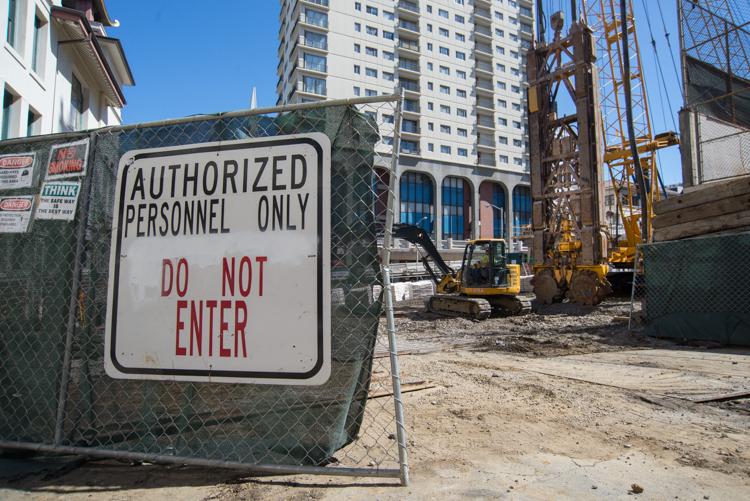 Construction site with authorized personnel only sign on chain-link fence, excavation equipment and building in background.