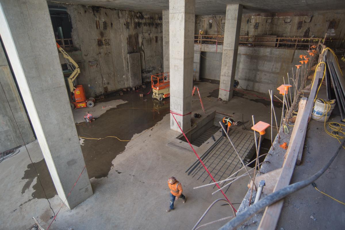 Construction workers installing rebar in escalator footing inside underground transit station headhouse.